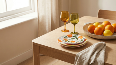 Borddækning med appelsintallerkener, farvede vinglas og fad med citrusfrugt