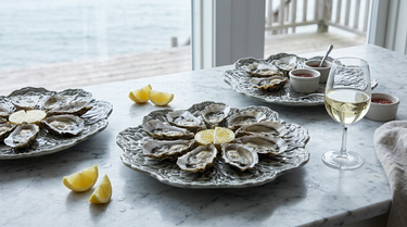 Østersfade i keramik formet som skaller med friske østers og citron på en marmorbordplade