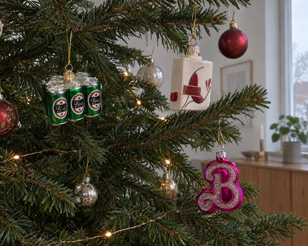 Roliga julkulor i glas formade som ett sexpack, ett vinpaket och ett rosa B i en julgran
